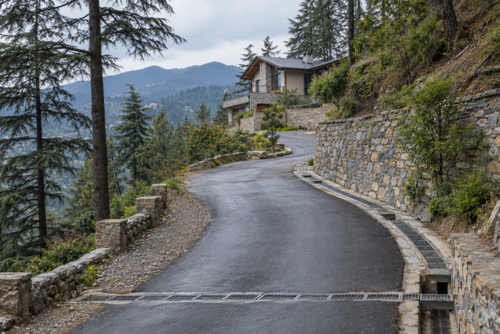 Mountain approach road with drainage and retaining wall near a Uttarakhand property